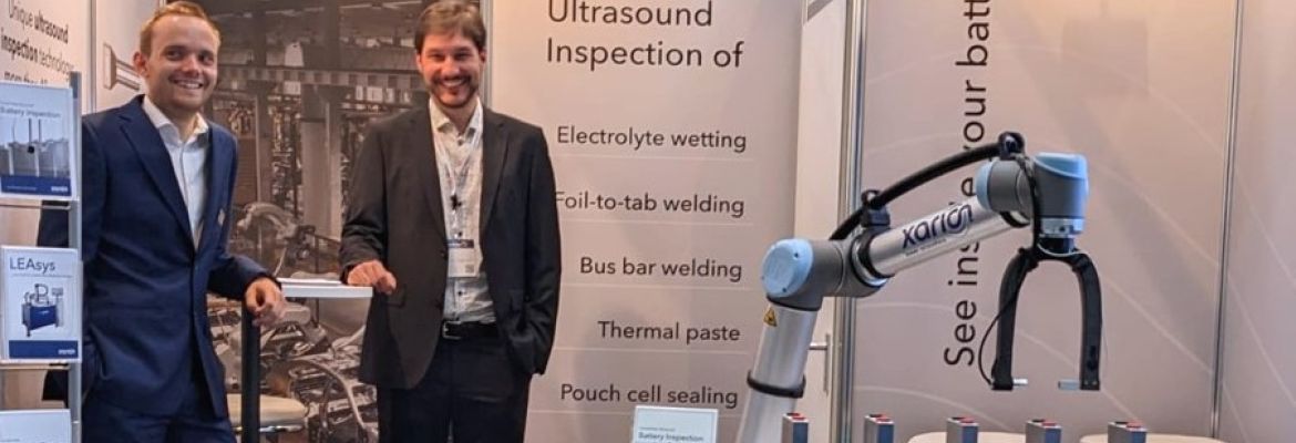 Zwei Personen sch&uuml;tteln sich die Hand neben einer XARION-Roboterpr&uuml;fzelle an einem Messestand